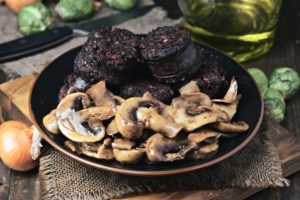 sliced mushrooms and blood sausage, fried in a porcelain dish on wood